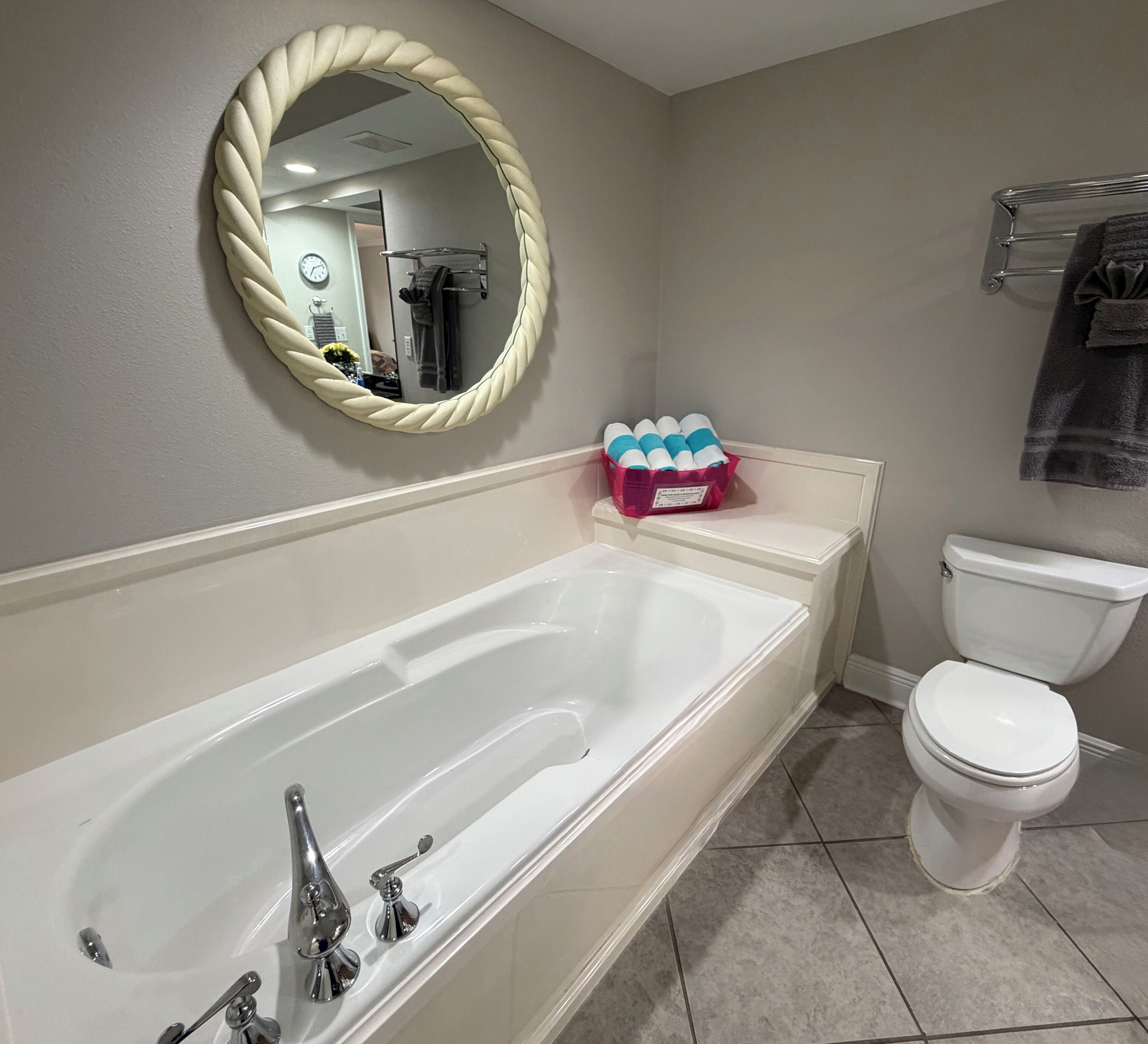 Une salle de bain comprenant une baignoire, des toilettes, un miroir orné d’un motif en forme de corde et un porte-serviettes.