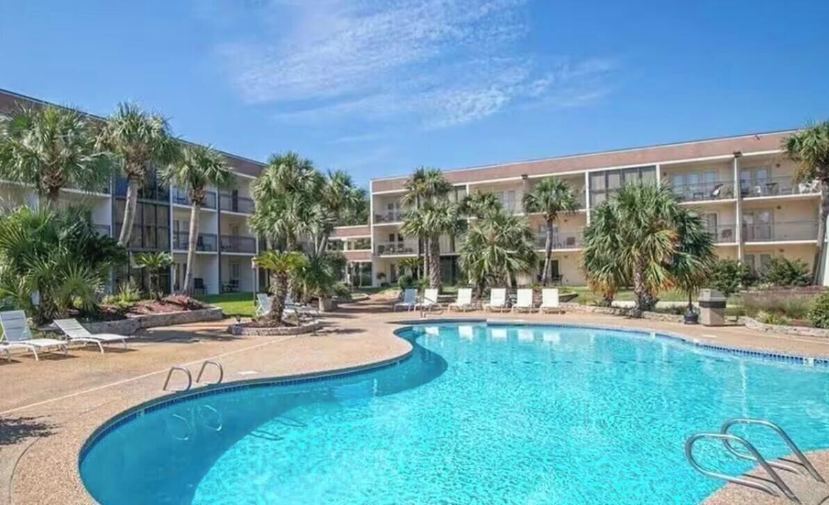 A hotel with a swimming pool, palm trees, and lounge chairs.
