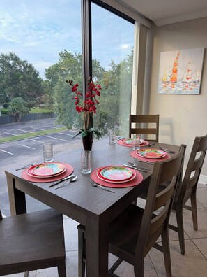 A dining table set with plates, cutlery, and glasses, with a window view of a parking lot and trees. - Safe & Sound (Biloxi)