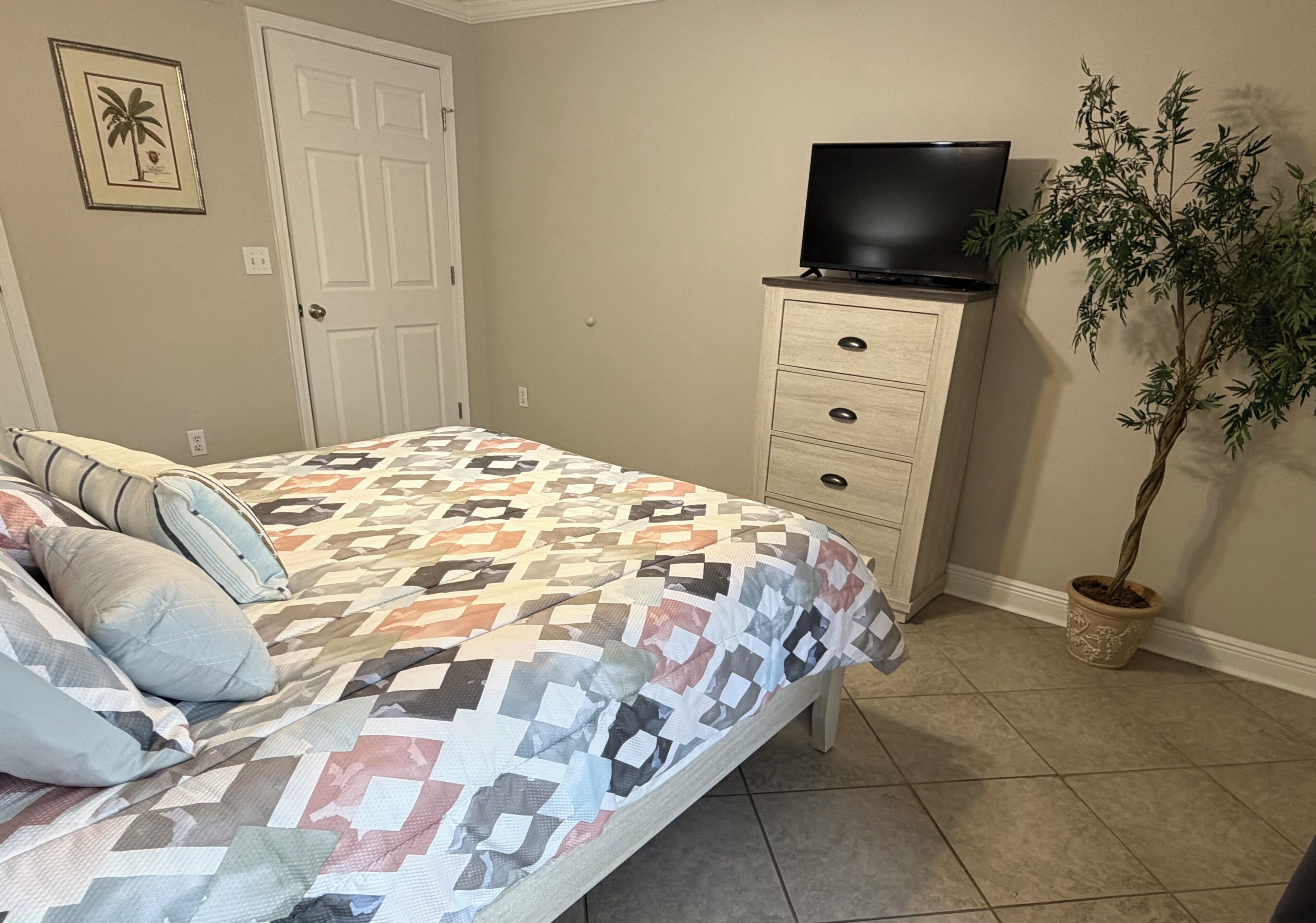 A bedroom with a bed, a dresser, a television, and a potted plant.