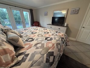 A bedroom with a bed, a television on a dresser, and a balcony with a view of trees. - Safe & Sound (Biloxi)