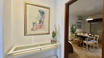 A hallway with a framed abstract painting, a white console table, and a dining area with chairs and a table set for a meal.
