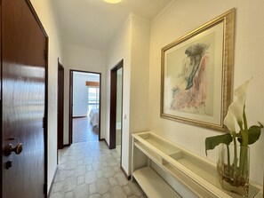 A hallway with a wooden door, a white bench, a framed artwork, and a vase with a plant. - Faro Central 1 by Homing (Faro)