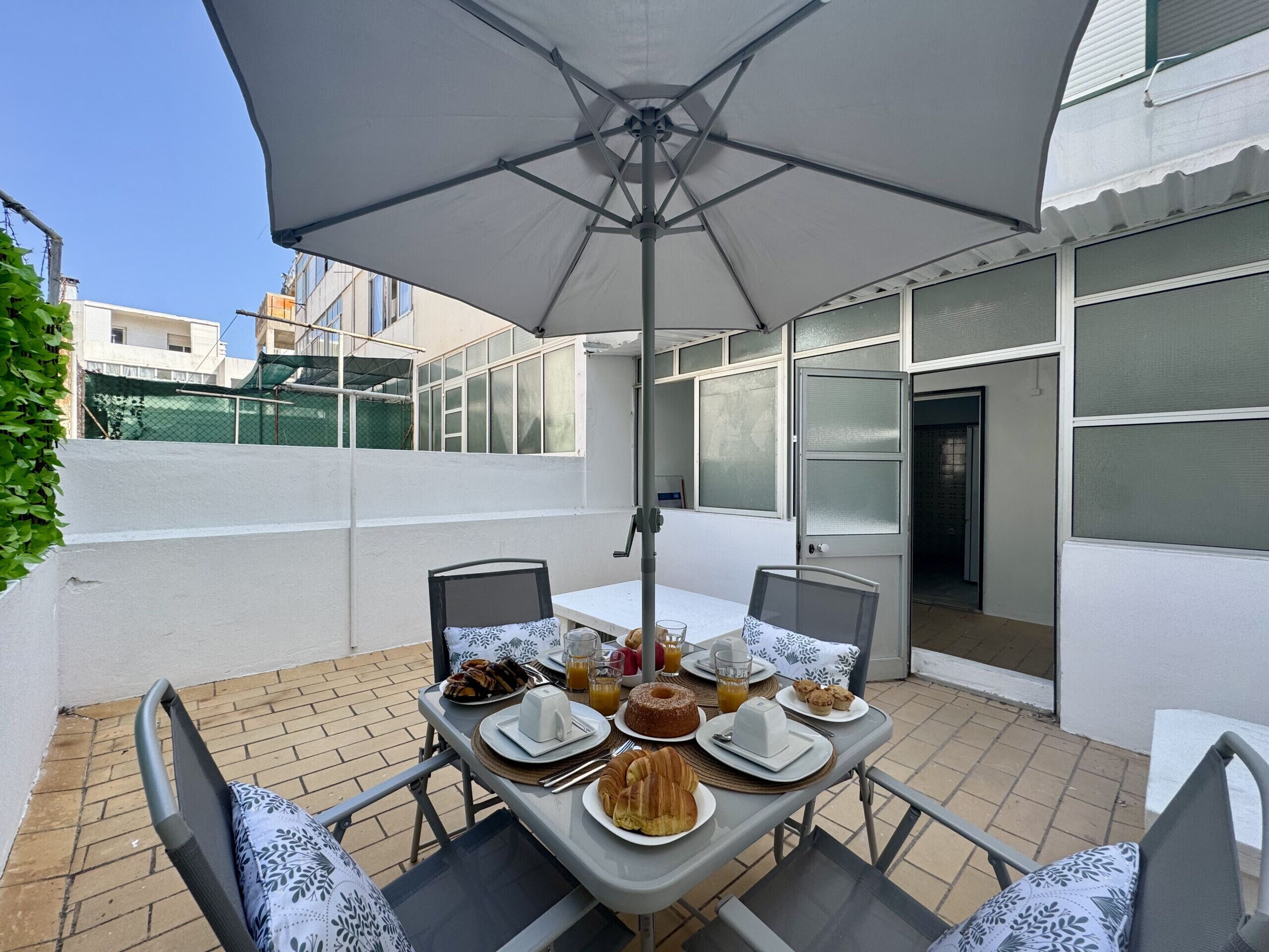 Un patio al aire libre con una mesa dispuesta para el desayuno, incluyendo croissants, un pastel y jugo.