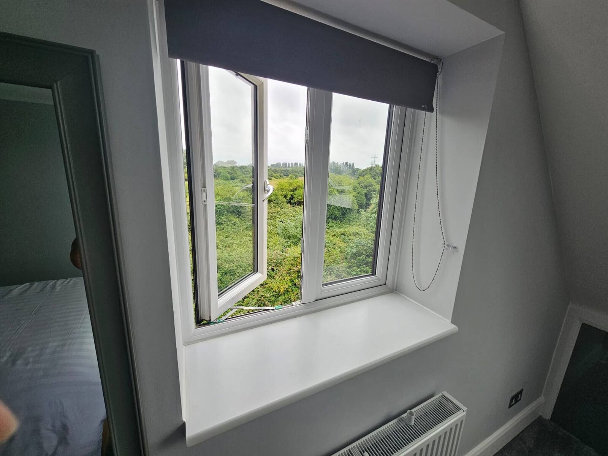 Habitación con ventana que da a un paisaje verde, radiador blanco debajo de la ventana y una puerta a la izquierda.