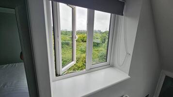 Habitación con ventana que da a un paisaje verde, radiador blanco debajo de la ventana y una puerta a la izquierda.