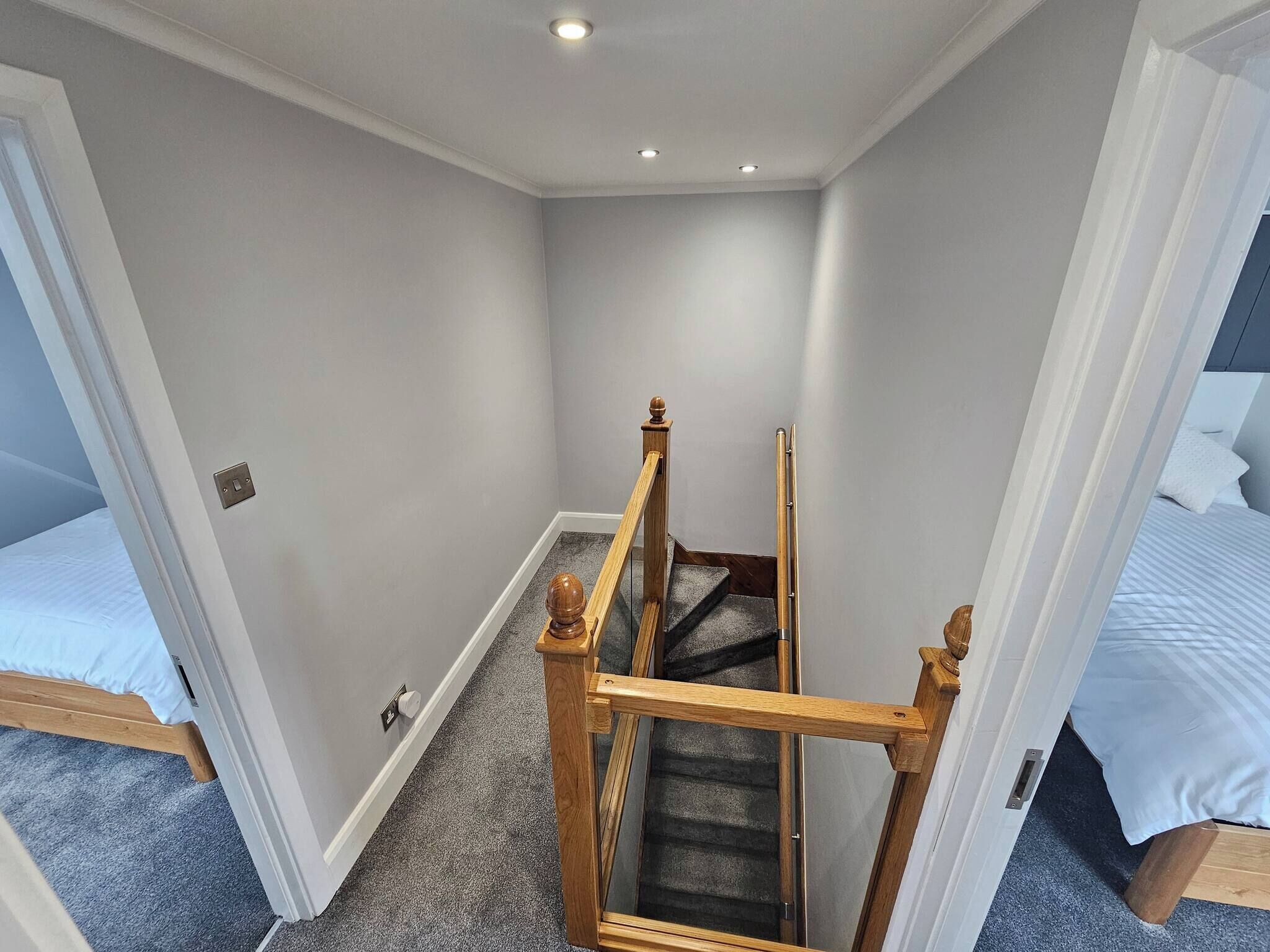 A narrow hallway with a wooden staircase leading to a bedroom.