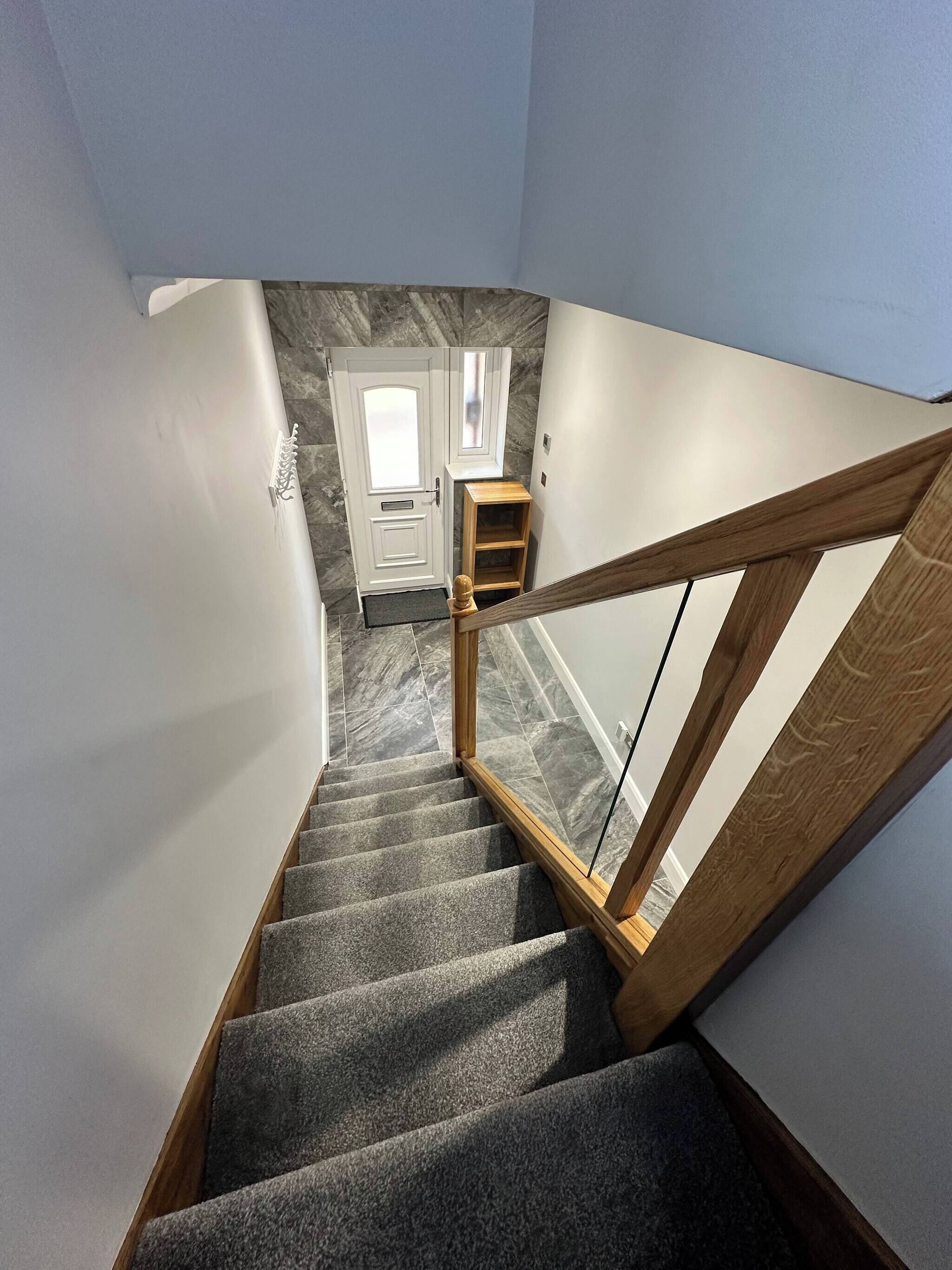 A staircase with a wooden handrail leading to a landing with a white door and a small wooden shelf.