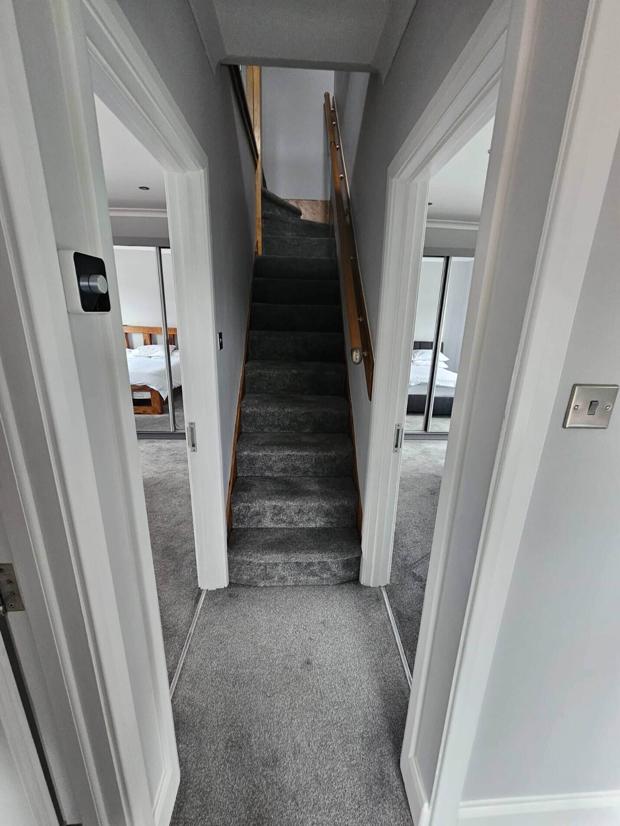 A narrow hallway with a carpeted staircase leading to a room with a bed.