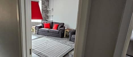 A modern living room with a grey sofa, red cushions, a patterned rug, and a stone-tiled floor.