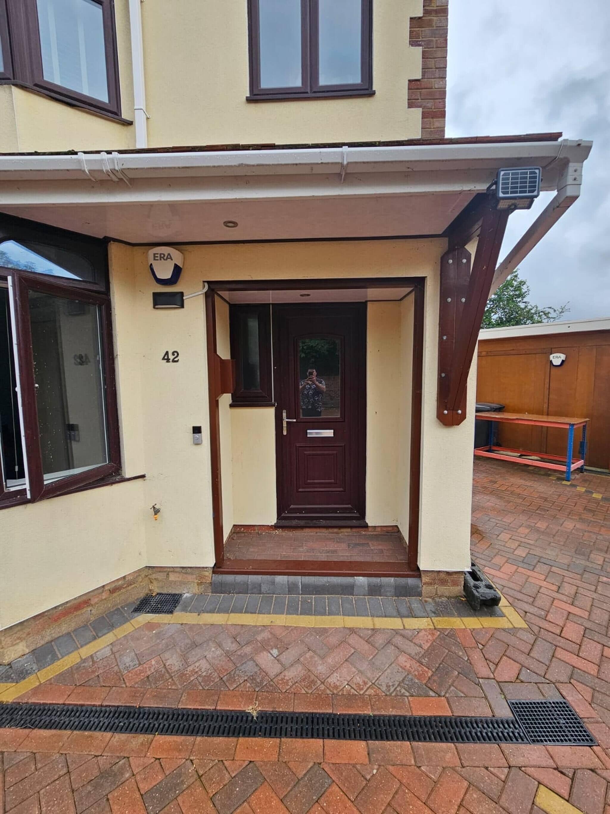 A residential entrance with a dark brown door, a small porch area, and a brick pathway leading to the entrance.