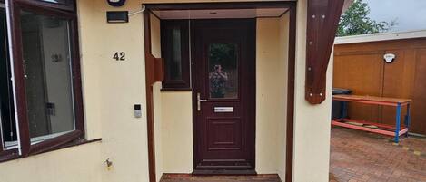Una entrada residencial con una puerta marrón oscuro, un pequeño porche y un camino de ladrillo que lleva a la entrada.