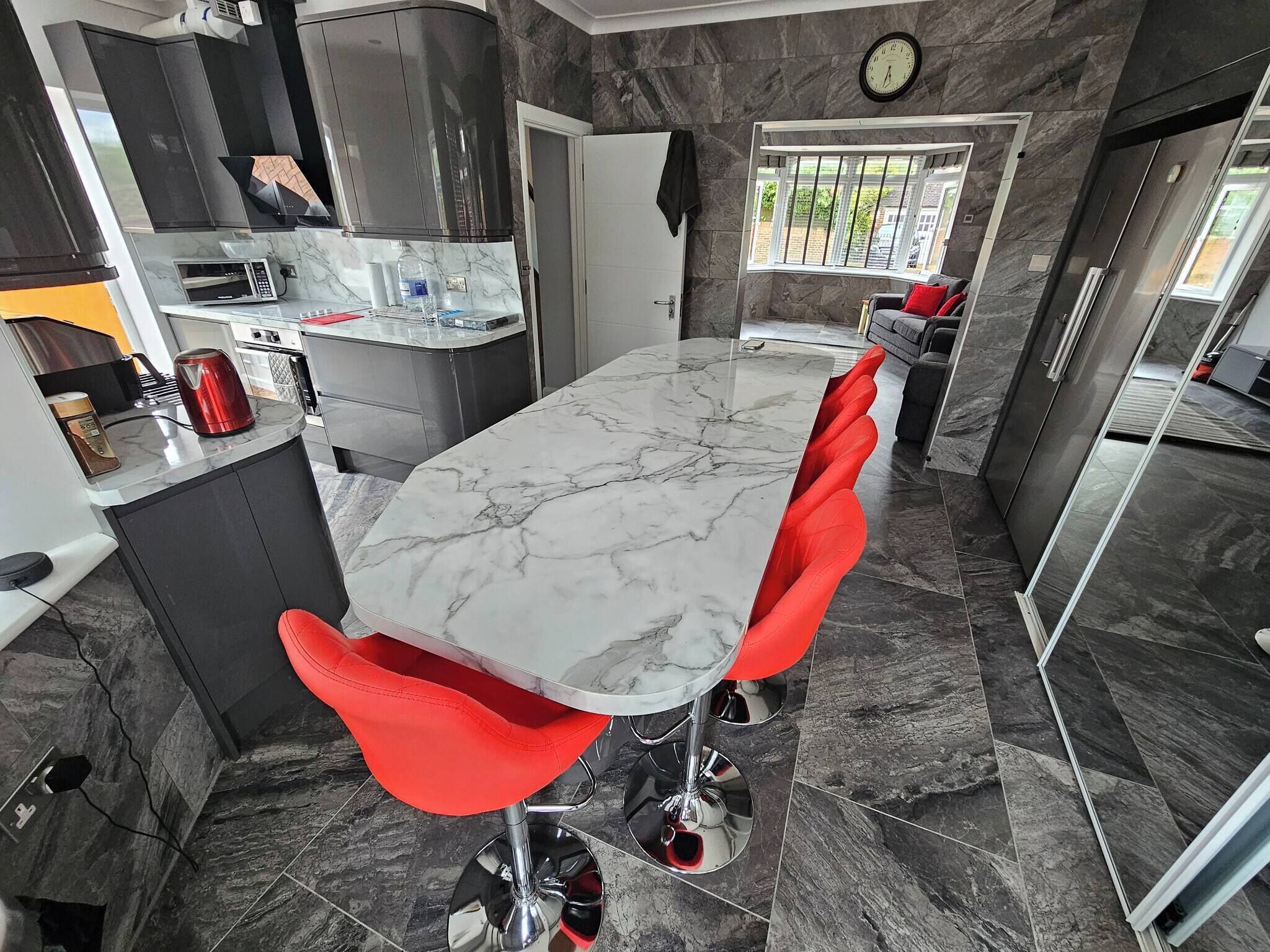 A modern kitchen with a marble countertop, red chairs, and a clock on the wall.