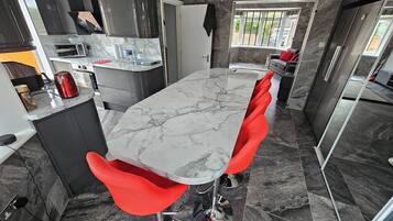 A modern kitchen with a marble countertop, red chairs, and a clock on the wall.