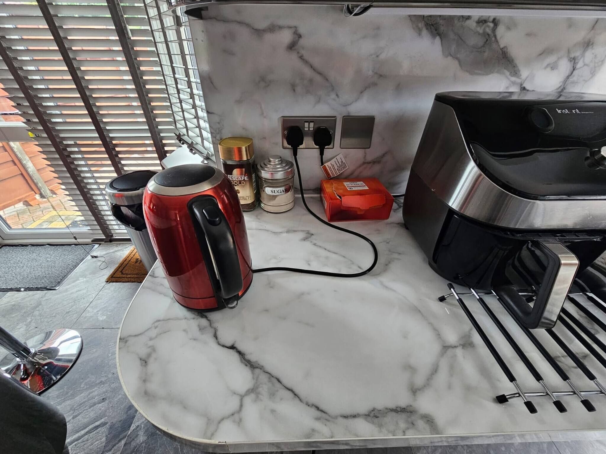 A kitchen with a marble countertop, a red kettle, a coffee maker, a sugar container, and a box of tea.