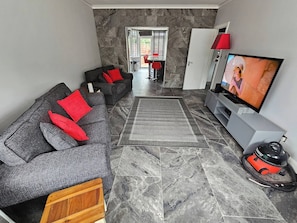 Una sala de estar moderna con un sofá gris, cojines rojos, un televisor y una aspiradora.