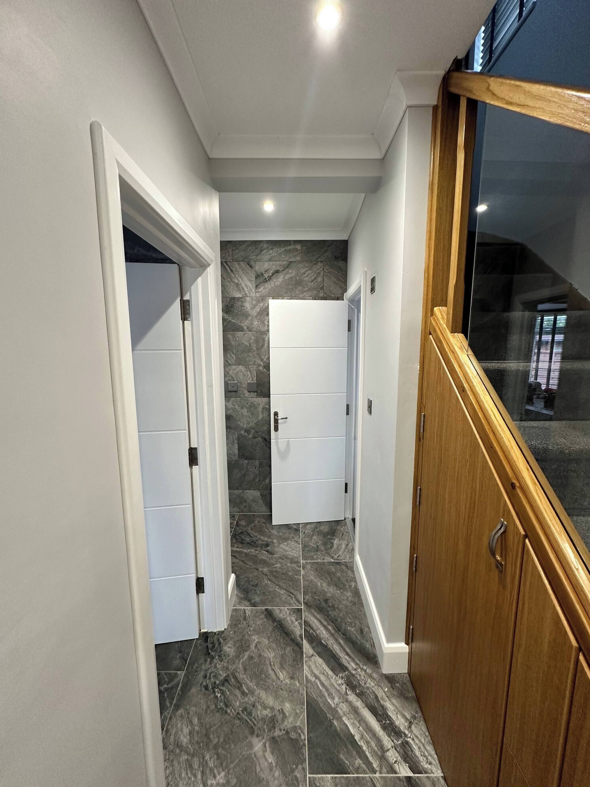 A hallway with marble flooring, white doors, and a wooden door frame.