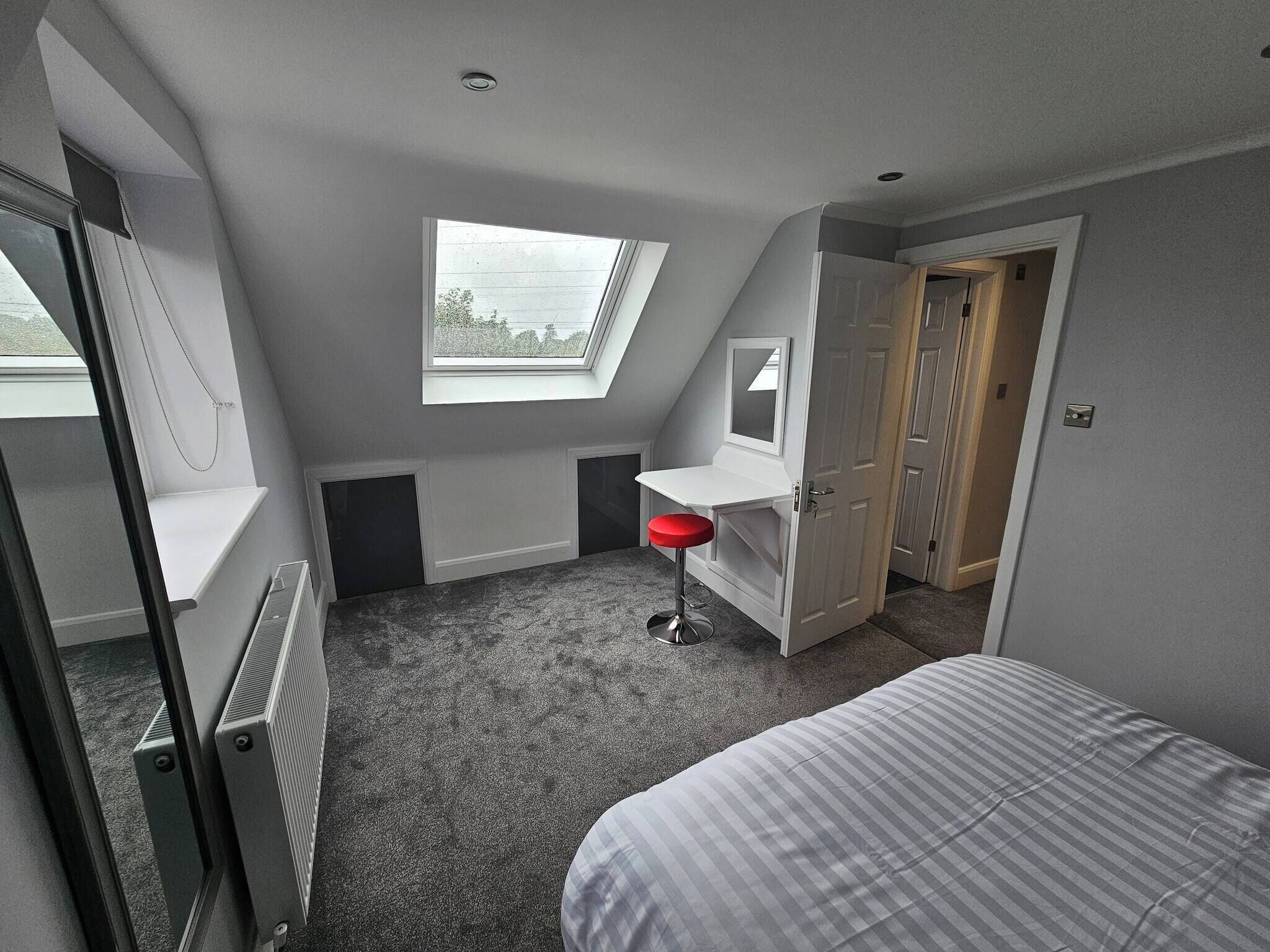 A bedroom with a skylight, a bed, a red stool, and a wardrobe.