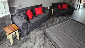 A modern living room with grey sofas, red cushions, a small wooden side table, and a patterned rug. - Serene 5-bedroom House in Staines-upon-thames With Garden (Staines)
