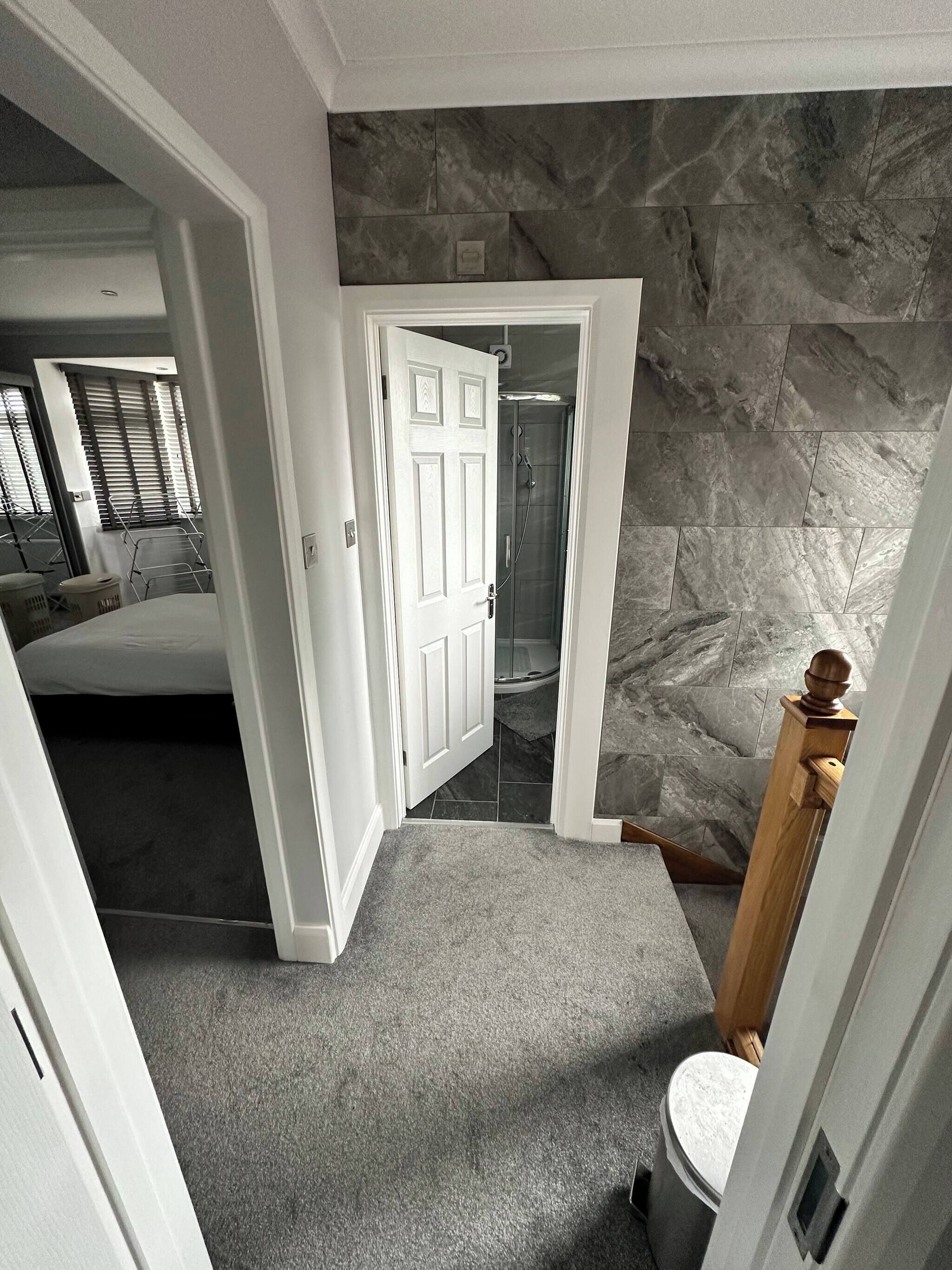 A hallway with a stone wall, a door leading to a bathroom, and a bedroom with a bed and a window.