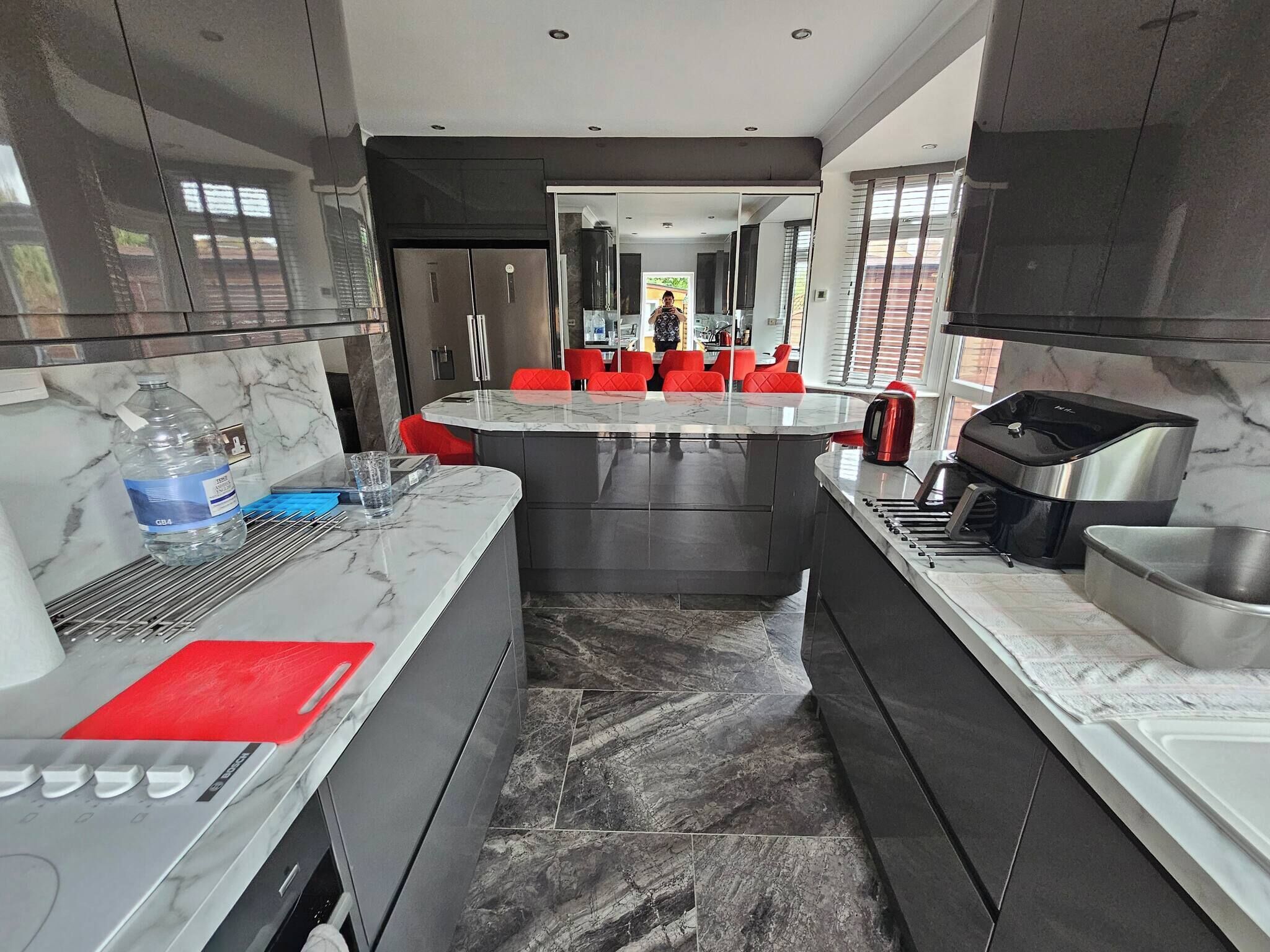 A modern kitchen with marble countertops, a central island, red chairs, and stainless steel appliances.