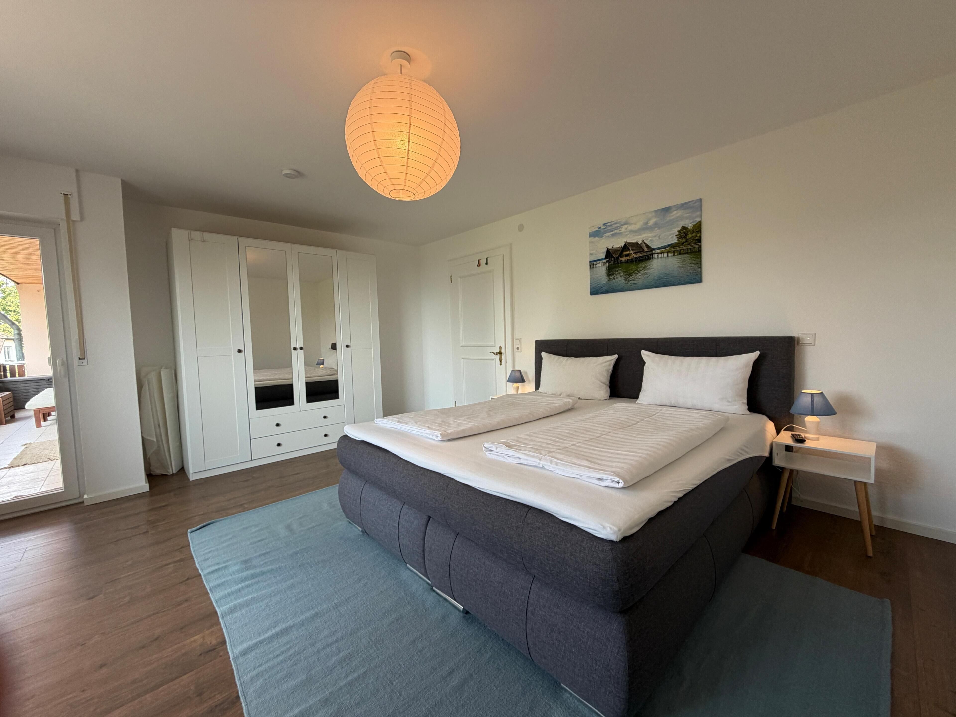 A bedroom with a large bed, a wardrobe, a nightstand, and a hanging light fixture.