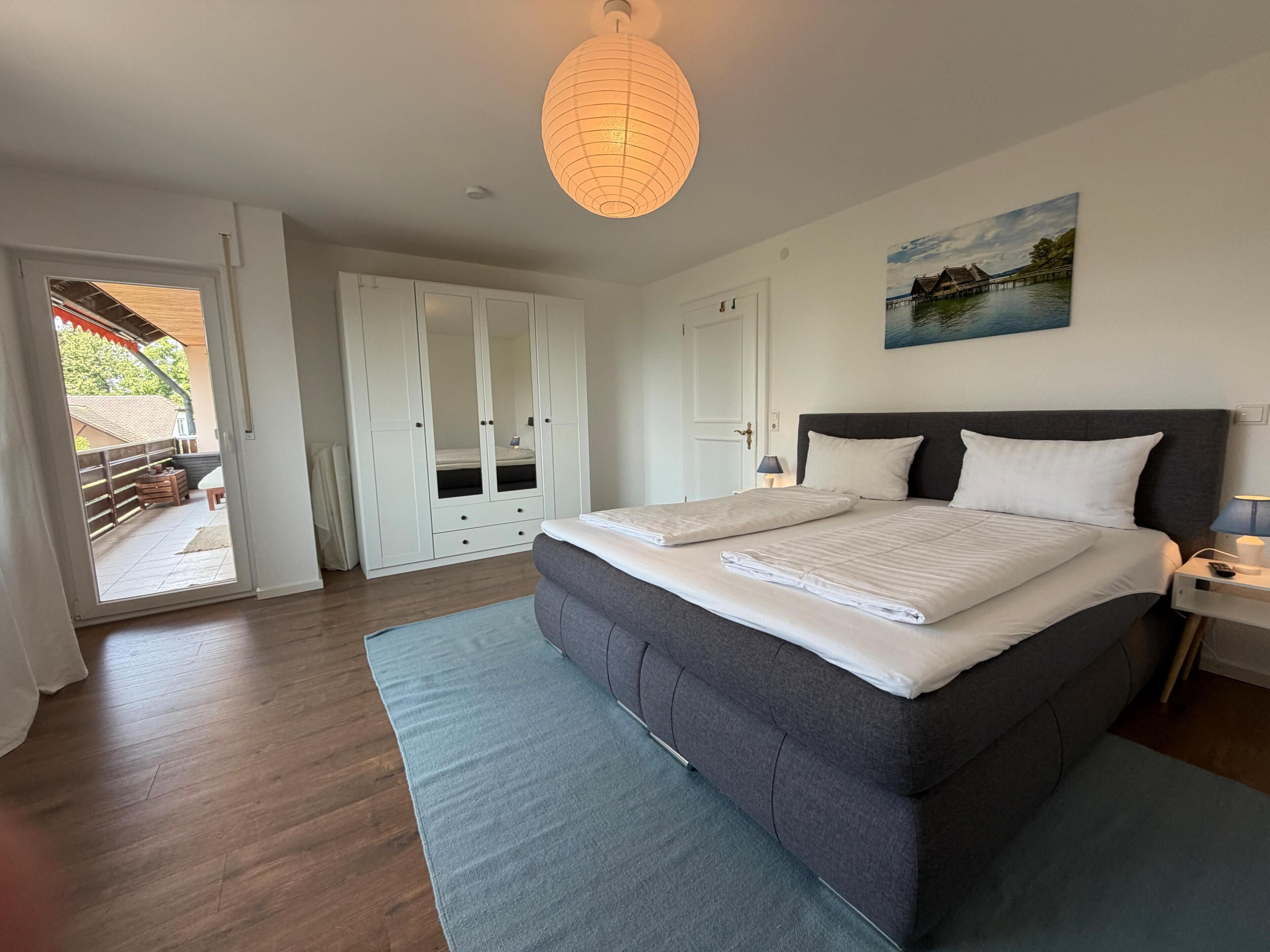 Een slaapkamer met een groot bed, een kledingkast, een schilderij en uitzicht op de omgeving.