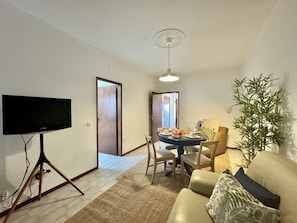A living room with a flat-screen TV, a dining table with chairs, a sofa, and a potted plant. - FARO CENTRAL 1 by HOMING (Faro)