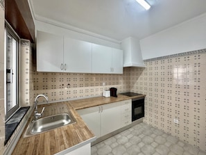 A kitchen with white cabinets, a wooden countertop, a stainless steel sink, a black dishwasher, and patterned backsplash tiles. - FARO CENTRAL 1 by HOMING (Faro)