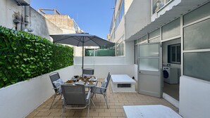 Eine Terrasse im Freien mit Tisch und Stühlen, einer grünen Wand und einem weißen Gebäude.