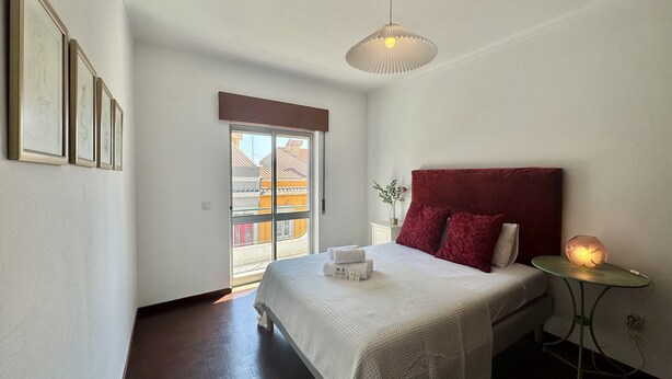 Ein Schlafzimmer mit Bett, Nachttisch mit Lampe, Fenster mit Blick und gerahmten Bildern an der Wand.