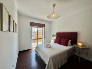Une chambre à coucher avec un lit, une table de chevet avec une lampe, une fenêtre donnant sur un beau paysage et des tableaux encadrés accrochés au mur.