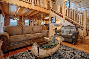 A wooden cabin interior with a living room, a dining area, and a staircase. - The Cats' Lair: Spectacular Views, Hot Tub, Wifi, Game Room, Resort Pool (Pigeon Forge)