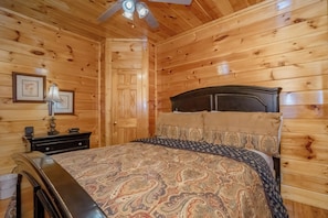 A wooden-paneled room with a bed, a nightstand, a lamp, and a door. - The Cats' Lair: Spectacular Views, Hot Tub, Wifi, Game Room, Resort Pool (Pigeon Forge)