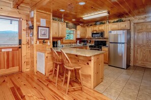 A wooden cabin interior with a kitchen area featuring a refrigerator, stove, microwave, and bar stools. - The Cats' Lair: Spectacular Views, Hot Tub, Wifi, Game Room, Resort Pool (Pigeon Forge)
