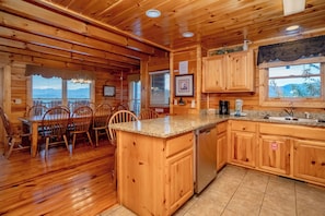 A wooden cabin interior with a dining area, kitchen, and large windows. - The Cats' Lair: Spectacular Views, Hot Tub, Wifi, Game Room, Resort Pool (Pigeon Forge)