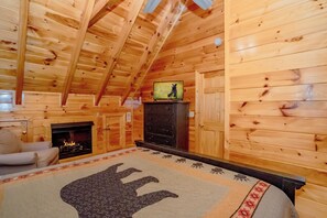 A log cabin interior with a fireplace, a television, and a bed with a bear design. - The Cats' Lair: Spectacular Views, Hot Tub, Wifi, Game Room, Resort Pool (Pigeon Forge)