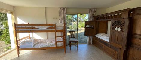 A room with bunk beds, a wooden cabinet, a chair, and a table.