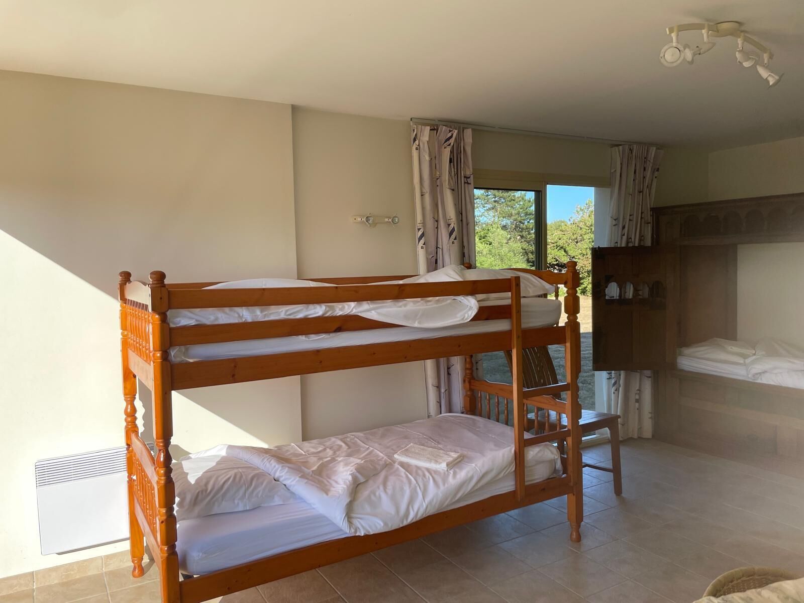 Une chambre avec un lit superposé, une fenêtre, des rideaux et une armoire.