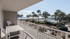 Ein Balkon mit Blick auf Pool und Strand, umgeben von Palmen.