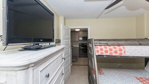 A compact room with a bed, a television, a kitchenette, and a door leading to another room. - C102 Low Floor, 3 Pools, Spectacular Sunset View (Panama City Beach)