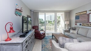 A living room with a sofa, a red lamp, a television, and a red leather chair. - C102 Low Floor, 3 Pools, Spectacular Sunset View (Panama City Beach)