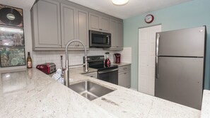 A kitchen with grey cabinets, a stainless steel refrigerator, a microwave, a sink, and a toaster. - C102 Low Floor, 3 Pools, Spectacular Sunset View (Panama City Beach)