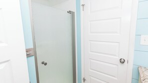 A bathroom with a white door, a shower area, and a towel rack. - C102 Low Floor, 3 Pools, Spectacular Sunset View (Panama City Beach)