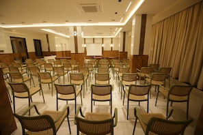 Un salón de conferencias con filas de sillas orientadas hacia una pizarra, una pantalla de proyector y un revestimiento de pared de madera.
