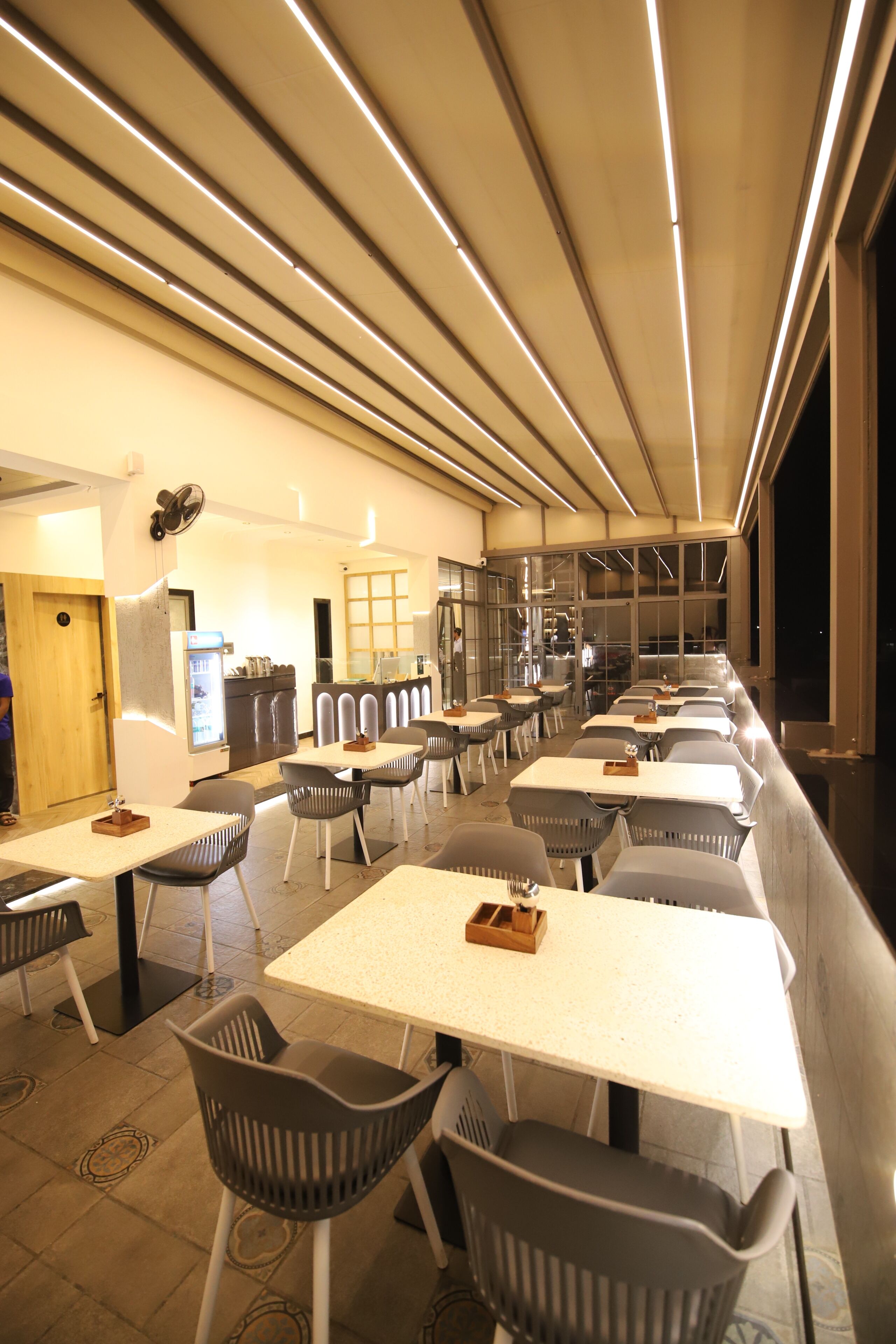 Un restaurante moderno con varias mesas y sillas, una zona de cocina y un amplio ventanal con vistas.