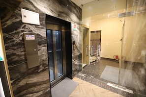 An elevator with a lift number sign, a marble wall, and a glass door leading to a hallway with a fire extinguisher.