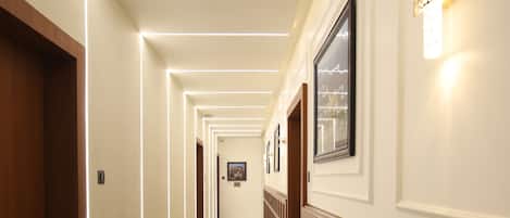 A hotel hallway with marble flooring, wooden paneling, and framed pictures on the walls.