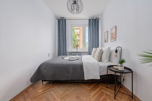 Ein Schlafzimmer mit Bett, Nachttisch, einer Topfpflanze und einem Fenster mit Vorhängen.