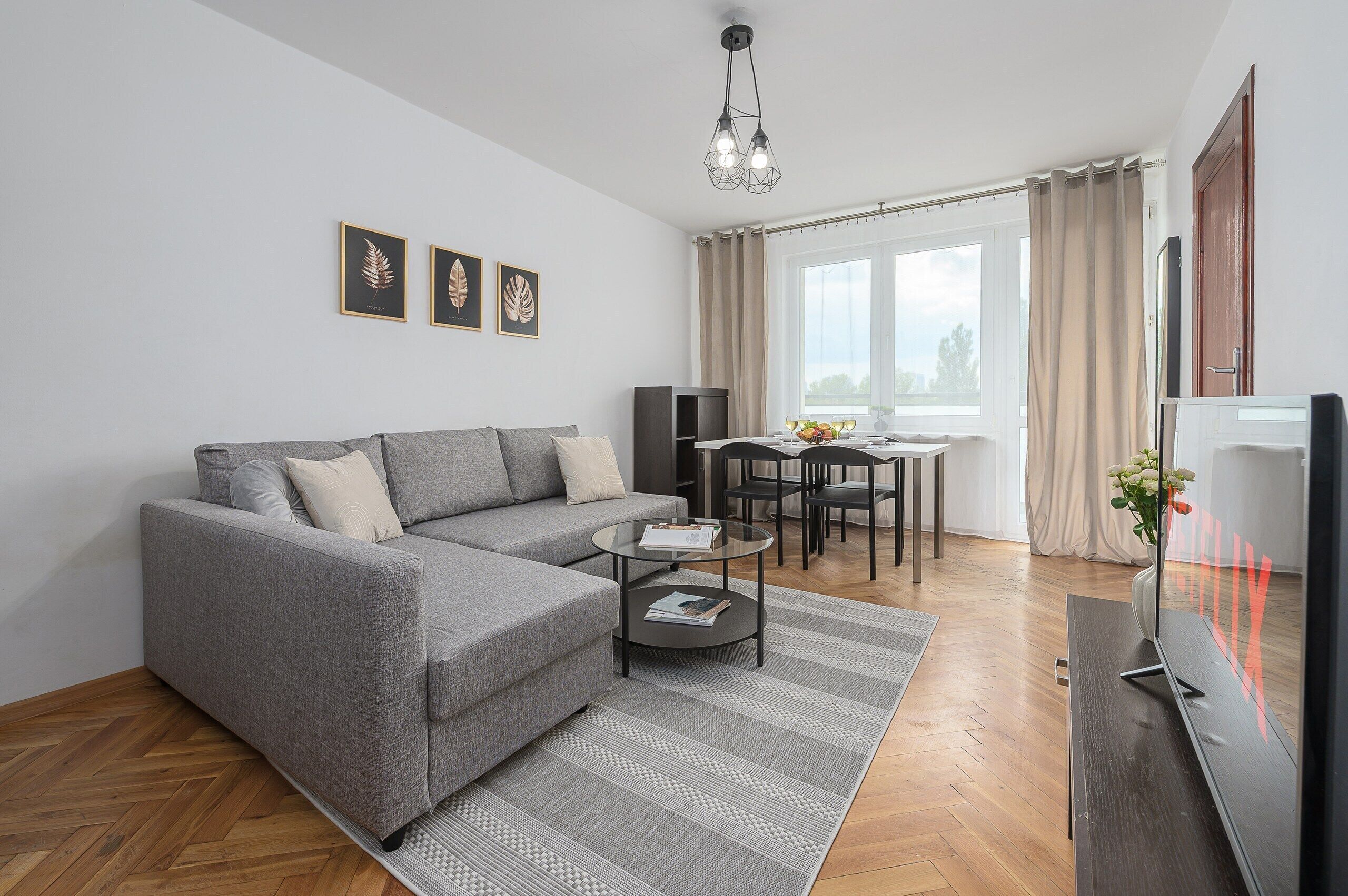 A modern living room with a grey sofa, a glass coffee table, and a dining area with chairs and a table.